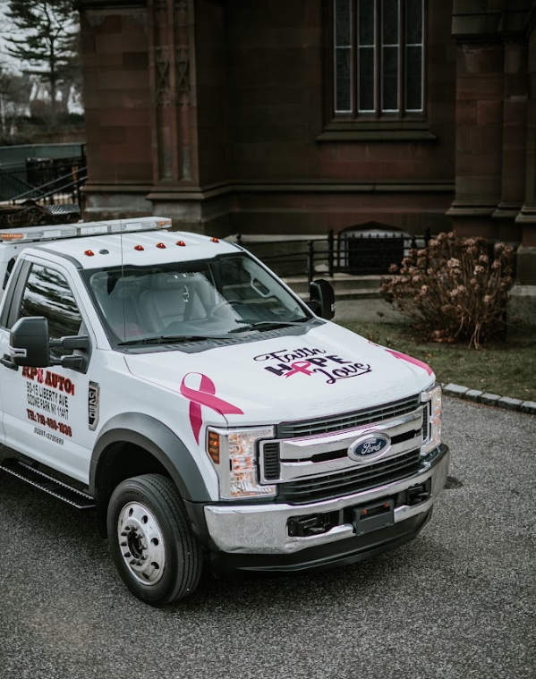 A white truck with a pink ribbon on the side is parked in front of a building.