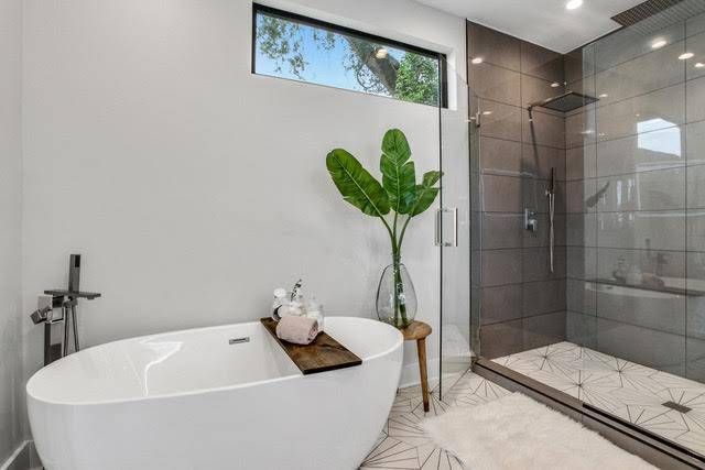 A modern bathroom featuring a white freestanding tub, a walk-in shower with gray tiles, and a potted plant.