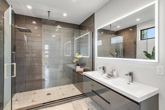 Modern bathroom with a glass-enclosed shower, geometric patterned floor tiles, brown tiled walls, and a double vanity.