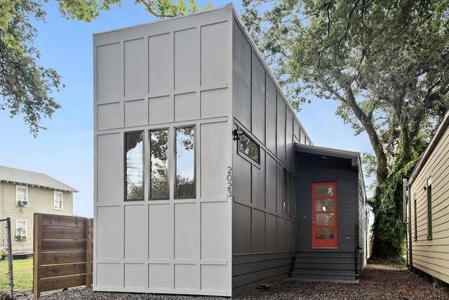 A modern, two-toned tiny house with white board-and-batten siding and a black side entrance with a bright orange door.