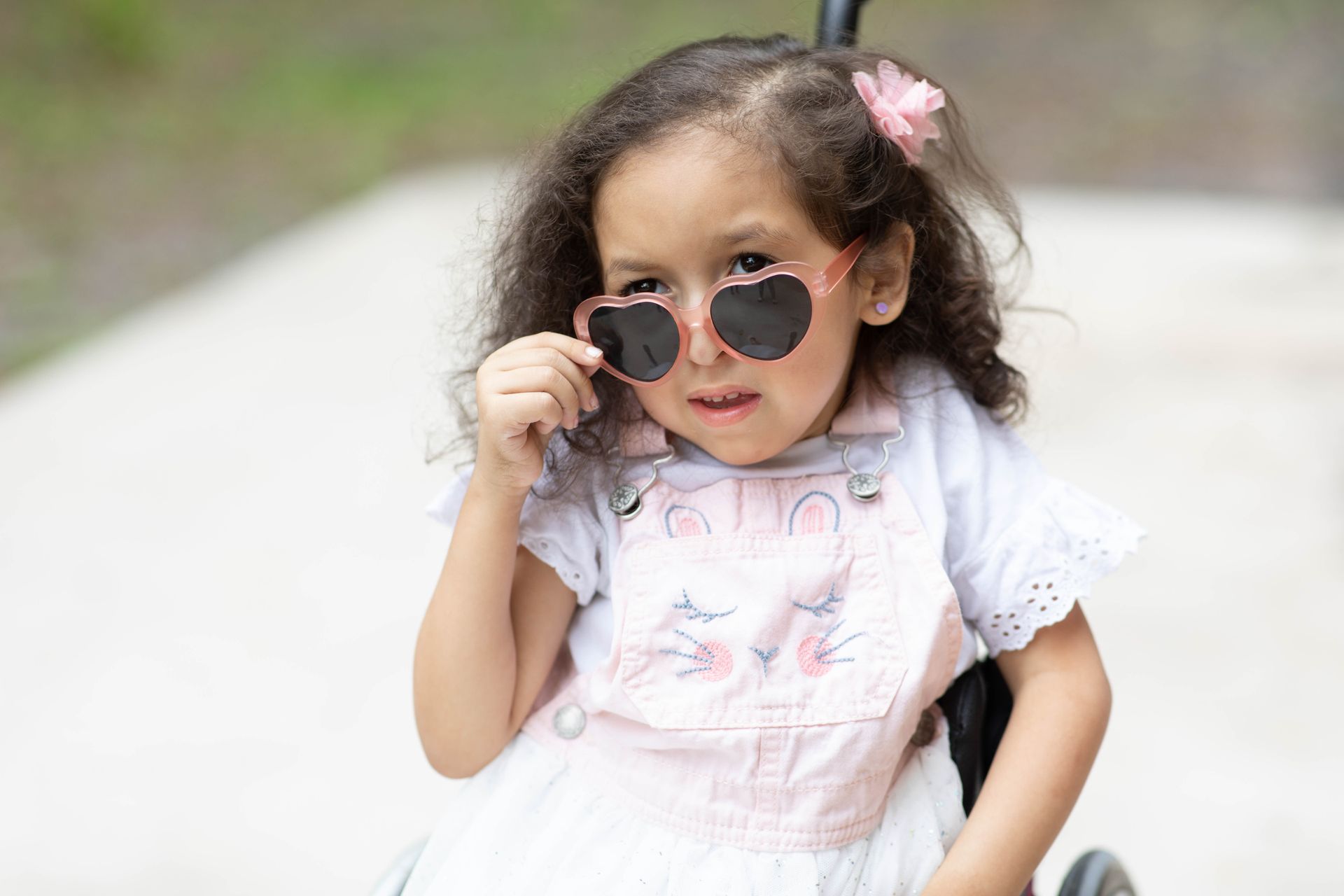 Young child in a pink dress adjusting round sunglasses outdoors