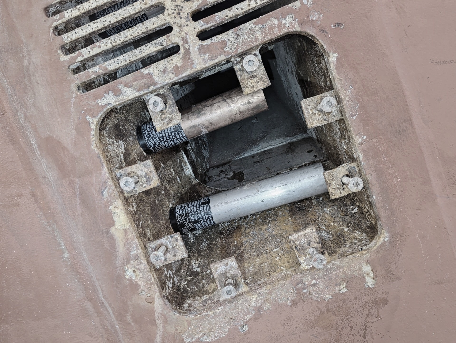 Close-up of an open rectangular vent on a reddish-brown surface. Shows metal tubes and supports inside.