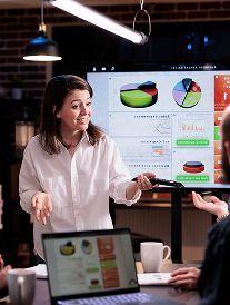 Woman presenting data on screen during meeting, using a remote.