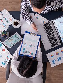 Two people reviewing charts and graphs at a desk with a laptop and tablet.