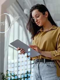 Woman with glasses uses a tablet, looking at data visualized with a circular 75% indicator.