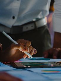 Person using a stylus to work on a tablet, possibly designing, with papers and a belt visible.