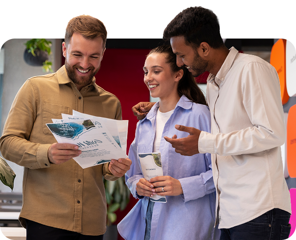 Three colleagues looking at printed materials; smiling in an office setting.