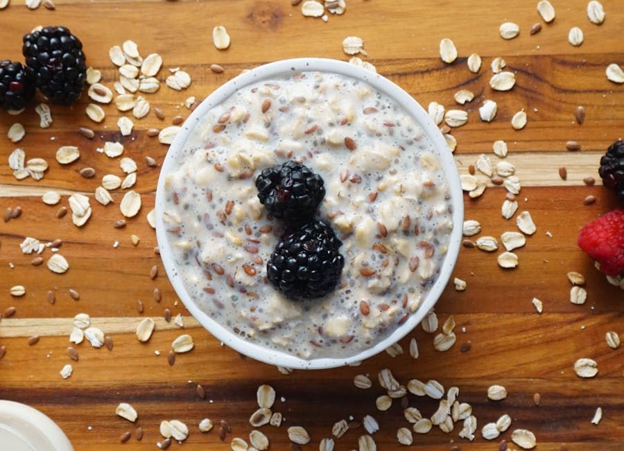 Bowl of oatmeal topped with blackberries and flaxseeds, surrounded by oats on a wooden surface, highlighting a fiber-rich meal option for GLP-1 patients.
