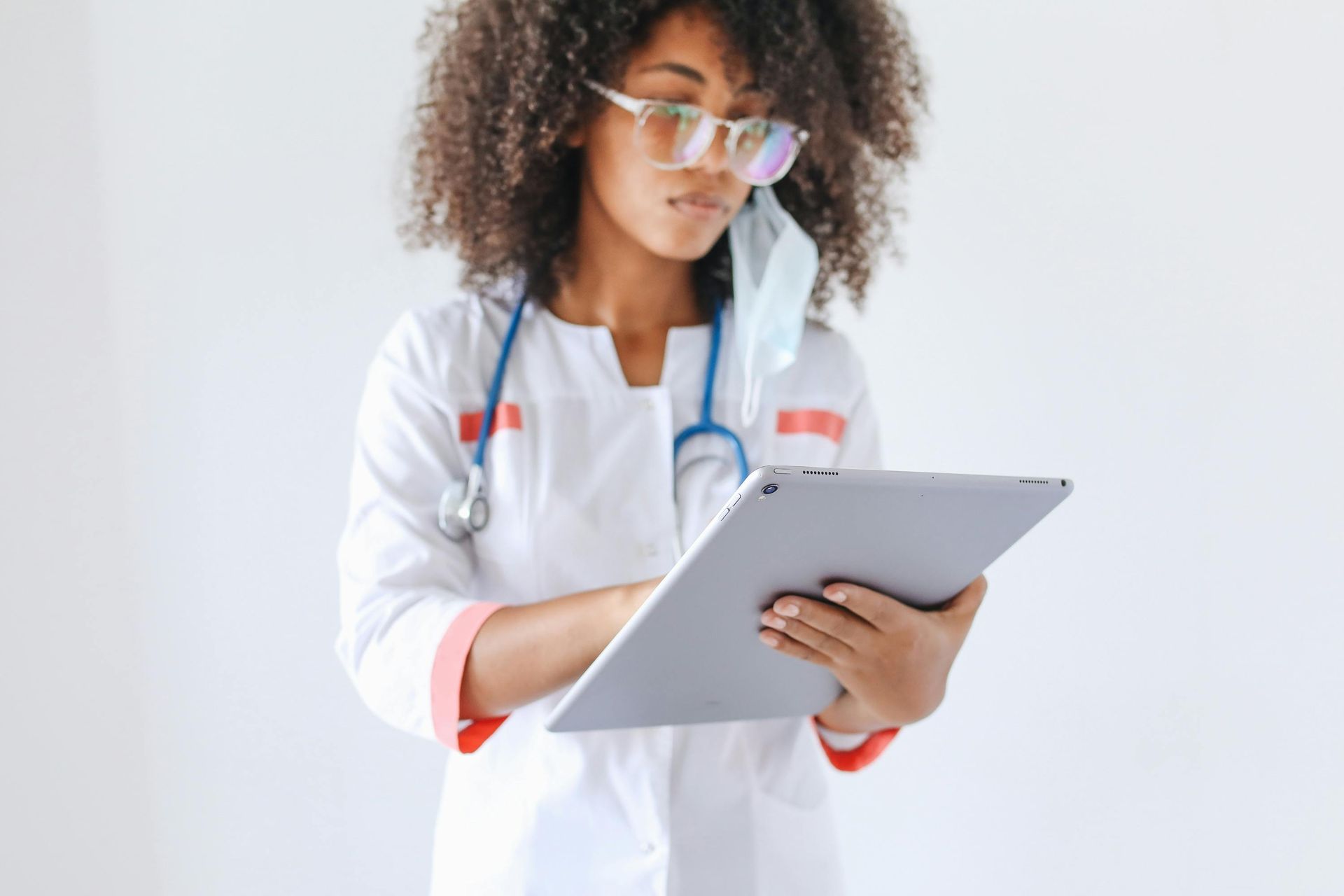 Healthcare professional in a white coat and stethoscope using a tablet, highlighting remote patient monitoring and care coordination in chronic disease management.