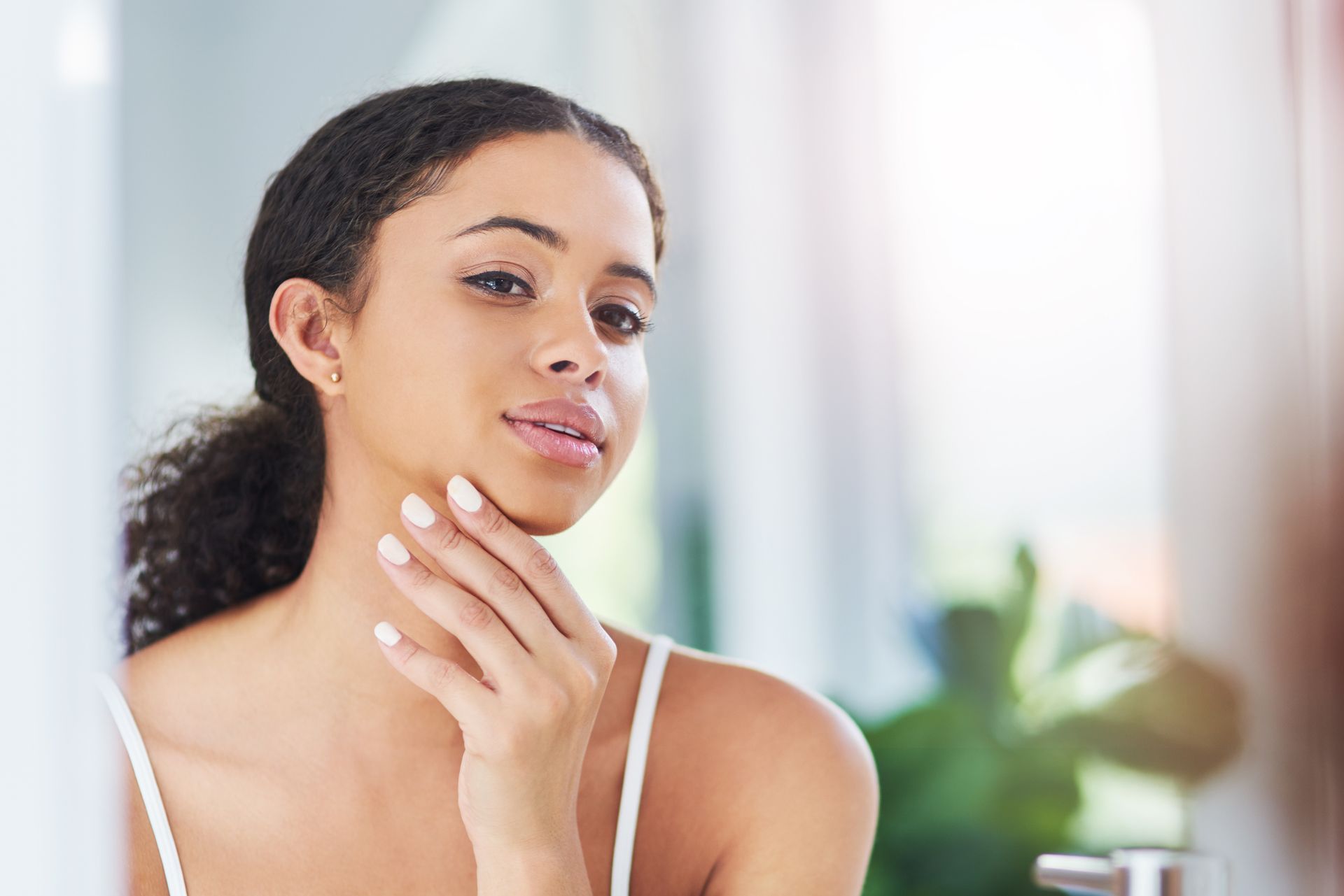 A woman is looking at her face in the mirror.