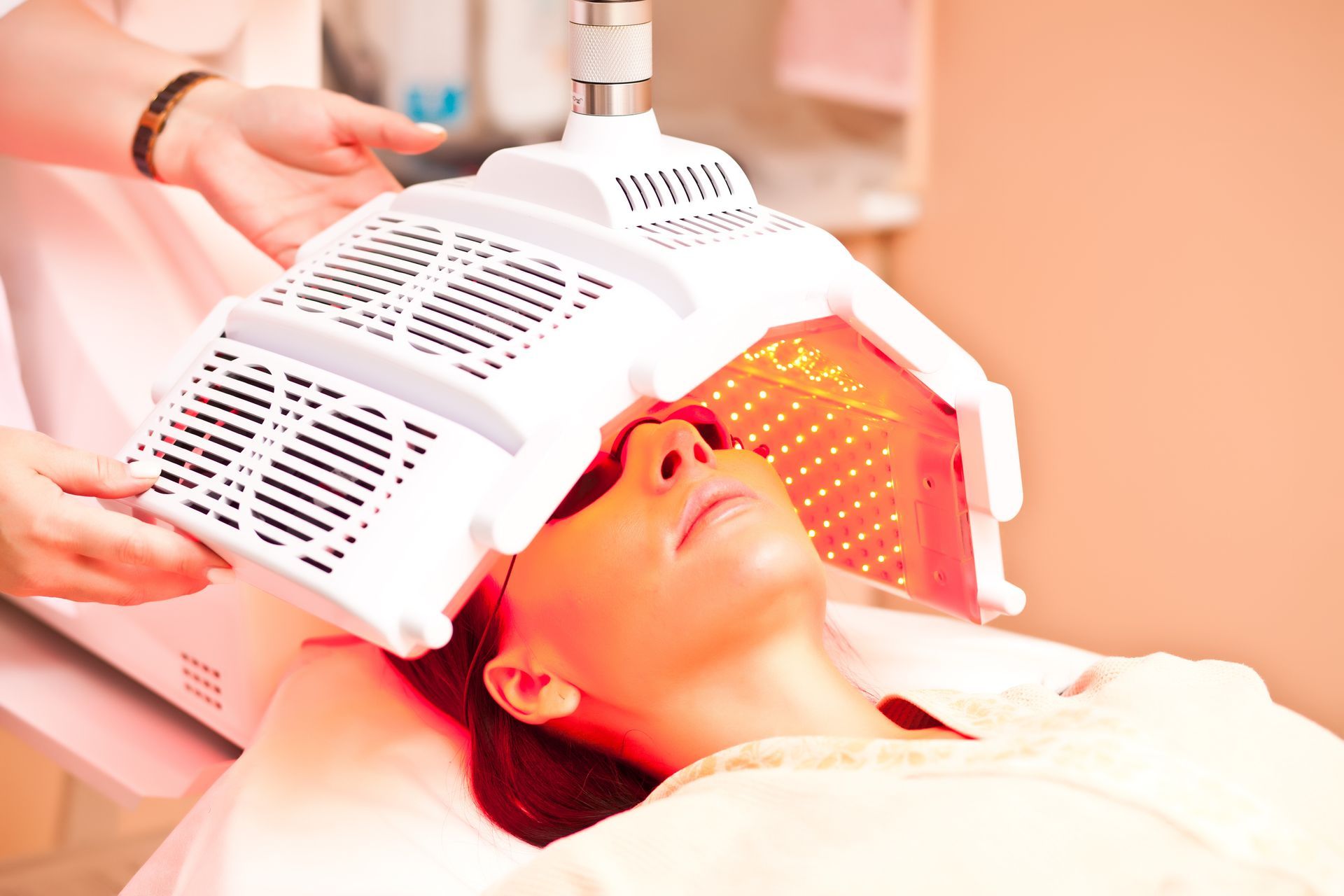Woman receiving red light therapy treatment at a spa, lying on a white bed.