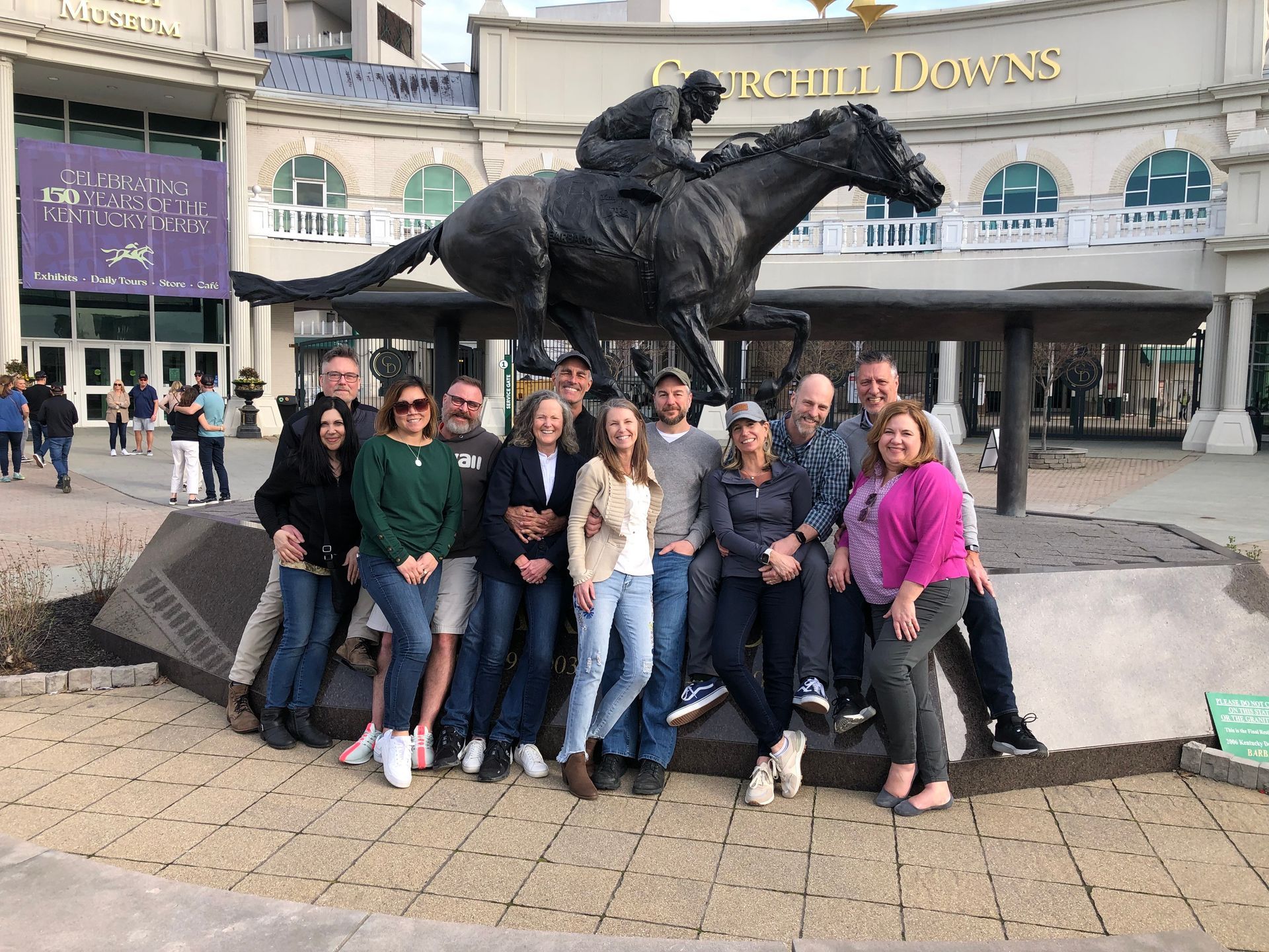 A group of people are posing for a picture in front of a statue of a jockey on a horse.