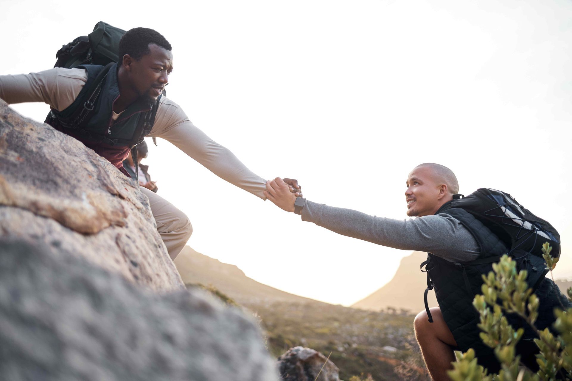 A man is helping another man climb a mountain.