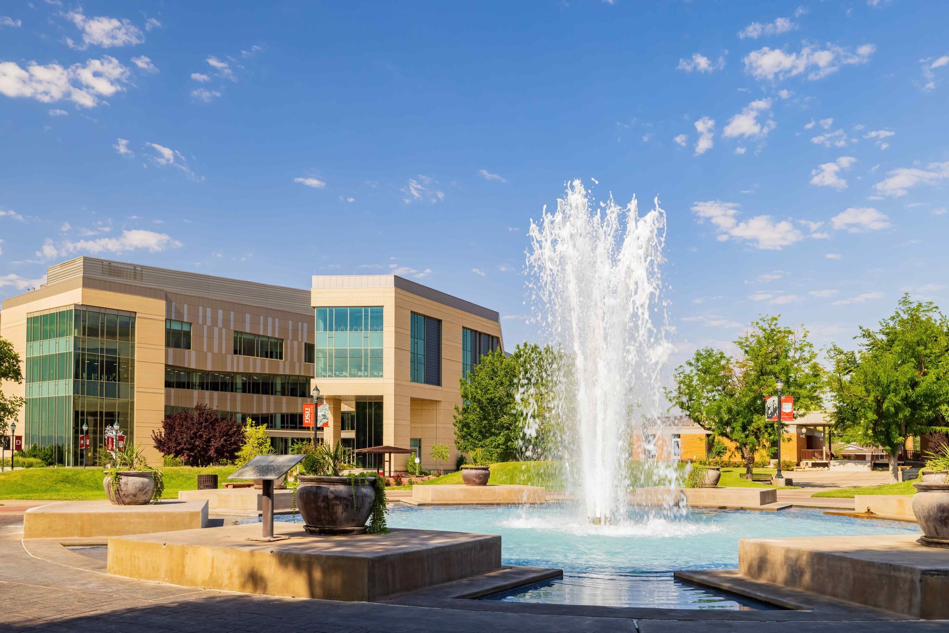 A large building, Dixie State University,  with a fountain in front of it.