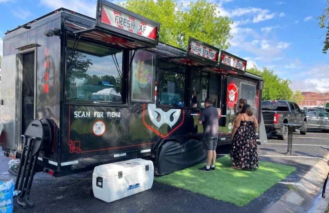 A food truck is parked in a St. George parking lot with people standing in front of it.