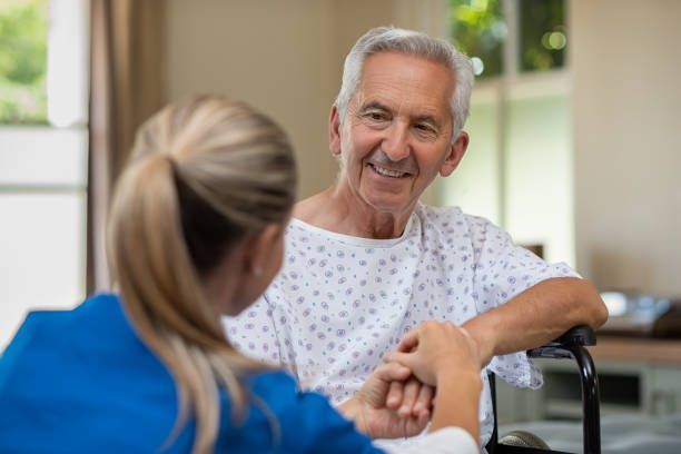 A nurse is holding the hand of an elderly man in a hospital gown - New City, NY - A & T Certified