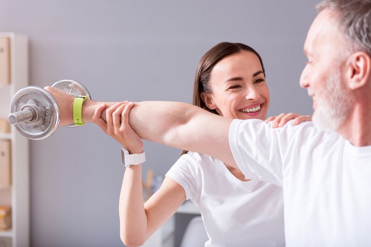 A woman is helping a man lift a dumbbell - New City, NY - A & T Certified