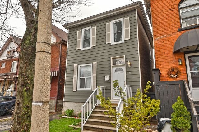 Two-story gray house with white shutters, steps leading to the front door, next to a brick building.