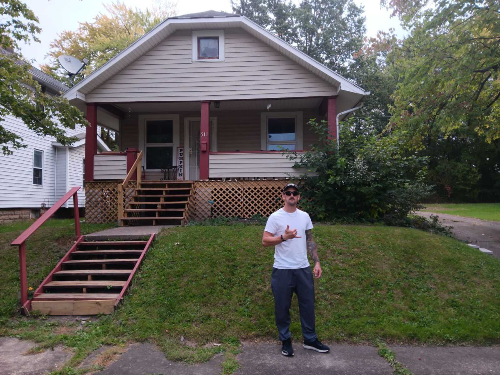 Man in front of small house, giving thumbs up. House has a porch, steps, and green grass.