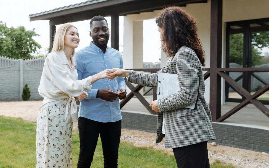 Couple shaking hands with a realtor outside a new home.