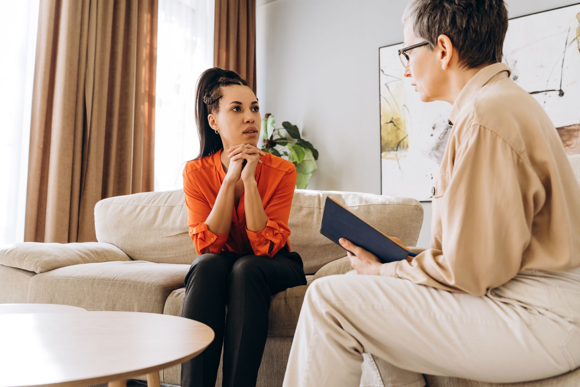 A woman is sitting on a couch talking to a woman.