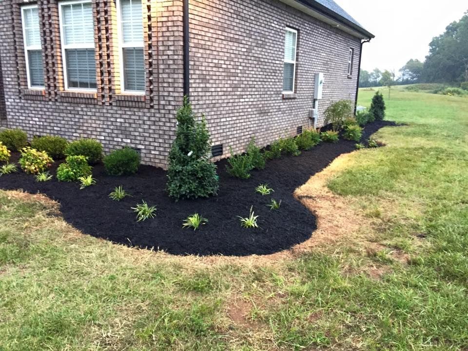 Brick house with a flower bed of plants and black mulch.