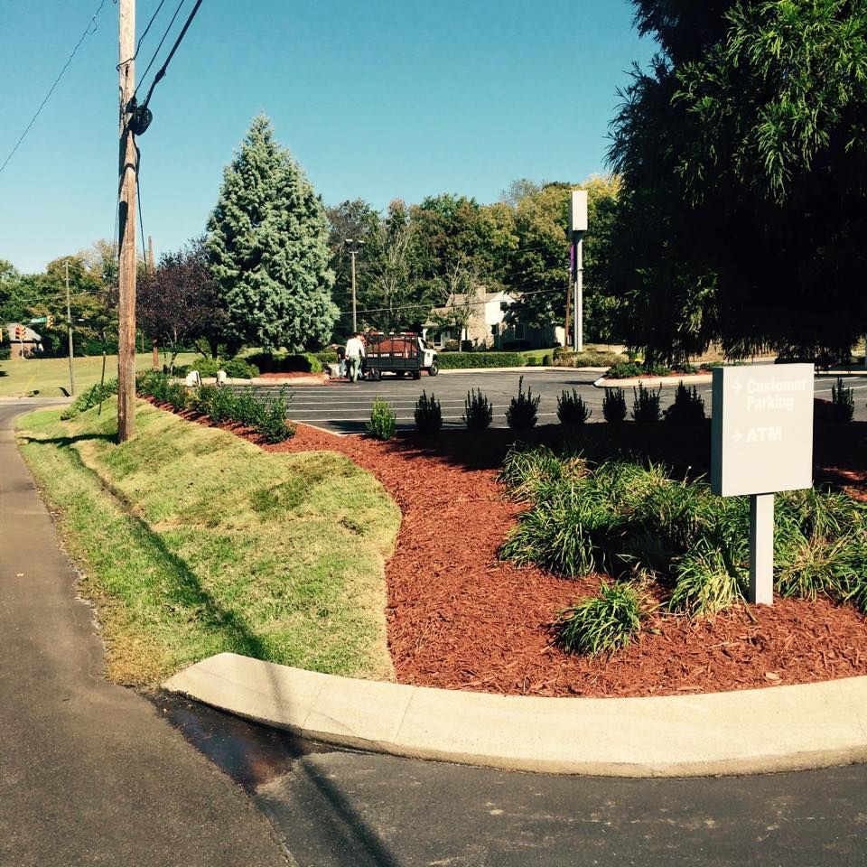 Landscaped area with red mulch, bushes, and a sign on a sunny day.