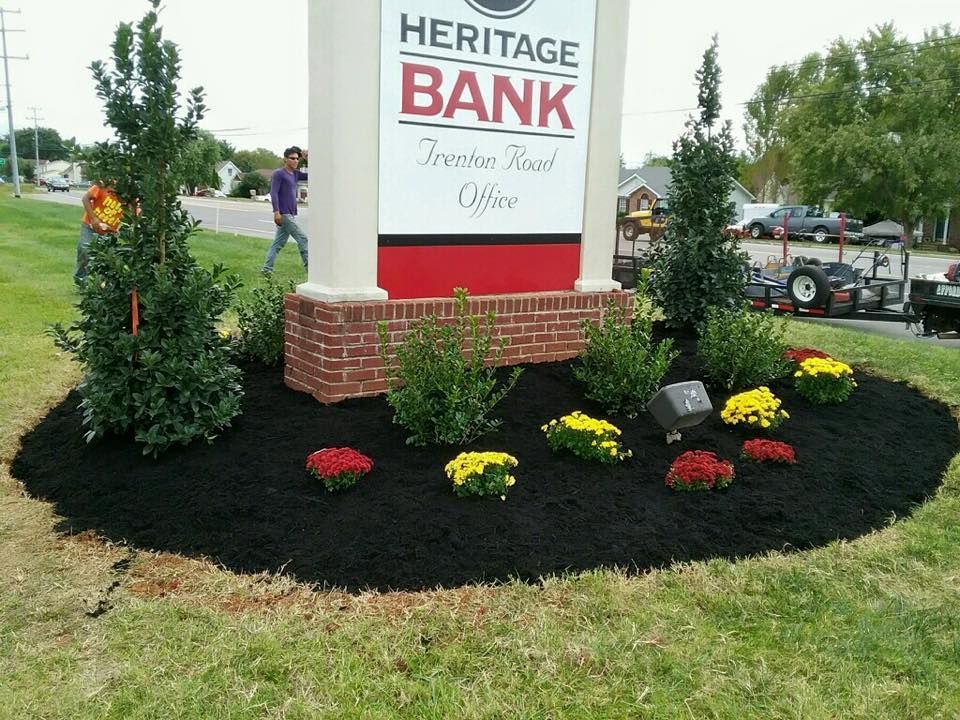 Heritage Bank sign with landscaped flower bed and workers.