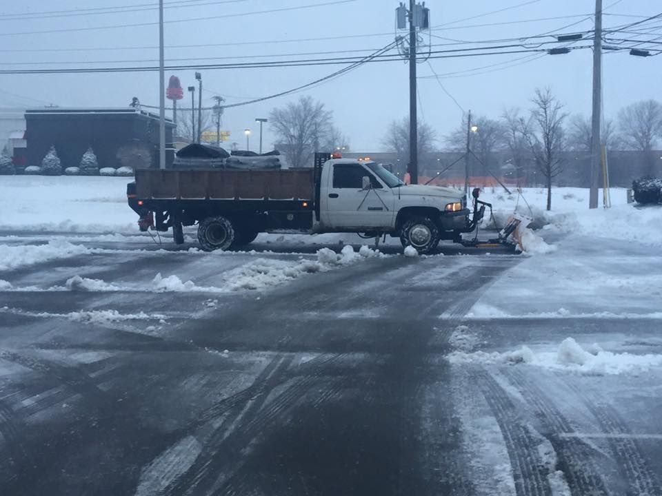 Snow plow truck clearing a parking lot during winter; overcast sky.