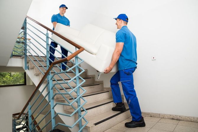 Two uniformed movers carrying a white sofa up a staircase.