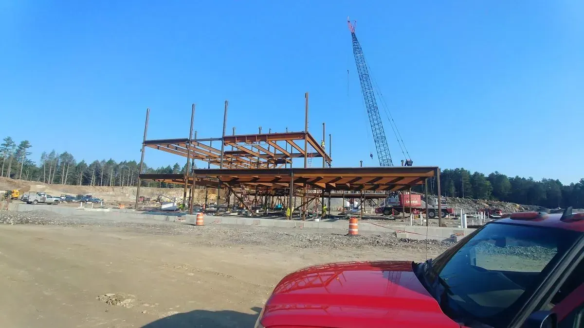 A red car is parked in front of a building under construction.