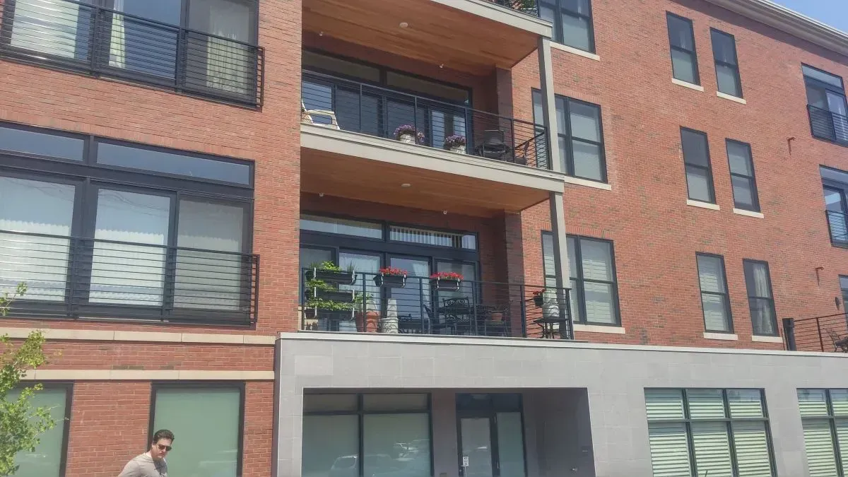 A man is standing in front of a large brick building with lots of windows.
