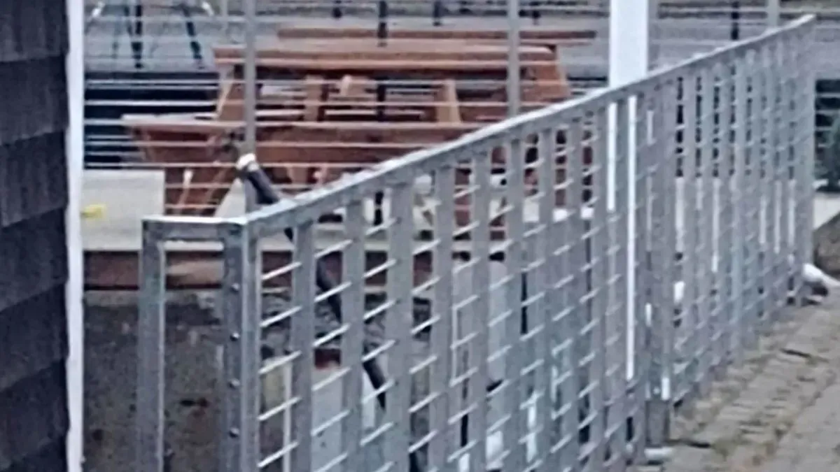A metal fence surrounds a deck with wooden picnic tables.