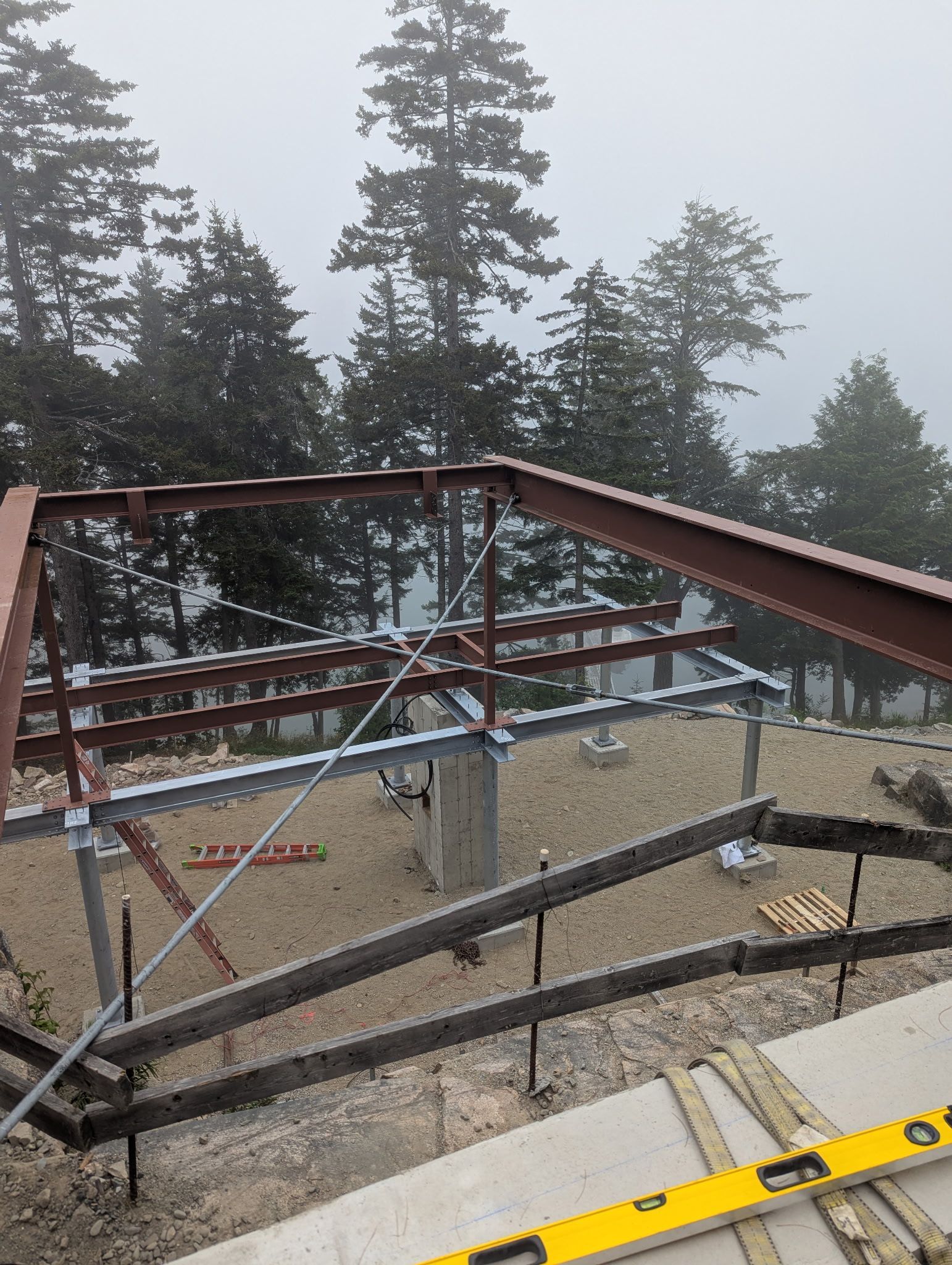 Steel beam framework of a building under construction on a foggy hillside, trees in the background.