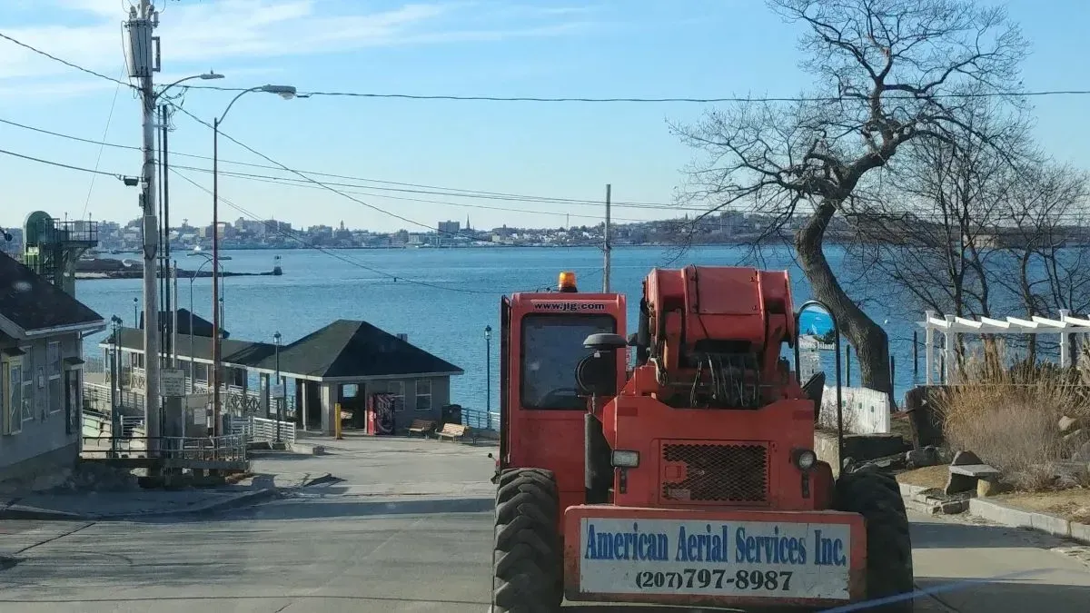 A red tractor is parked on the side of the road in front of a body of water.