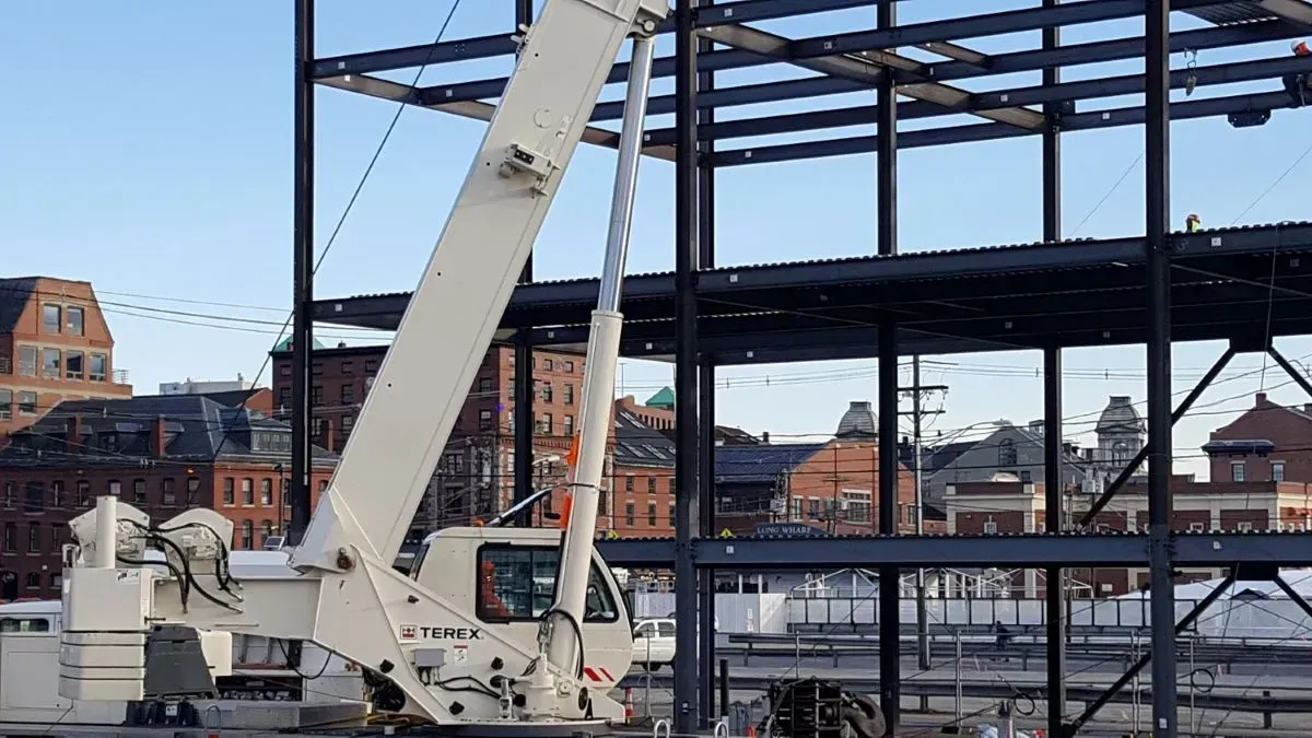 A large white crane is sitting on top of a building under construction.