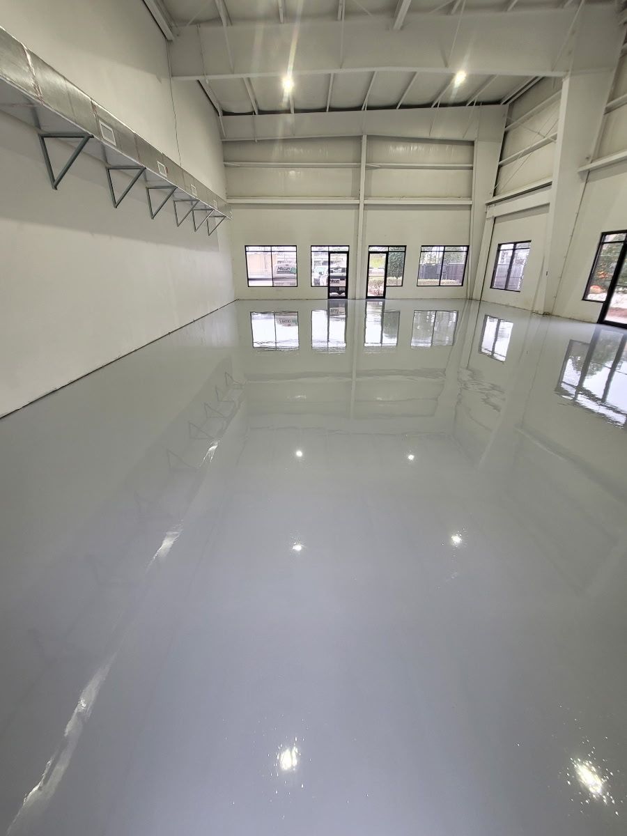 Person kneeling, smoothing epoxy coating on a gray floor with a trowel, wearing gloves.