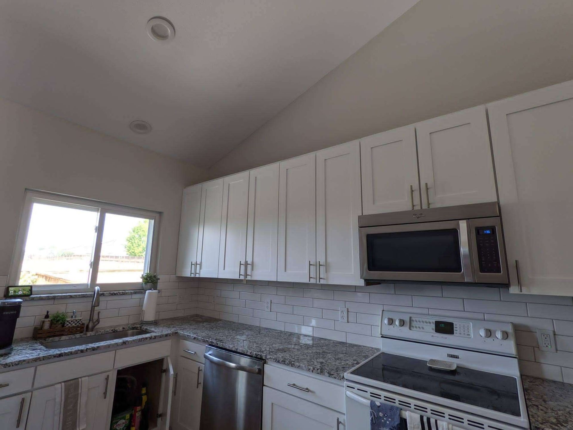 White kitchen with cabinets, stainless steel appliances, and a window.