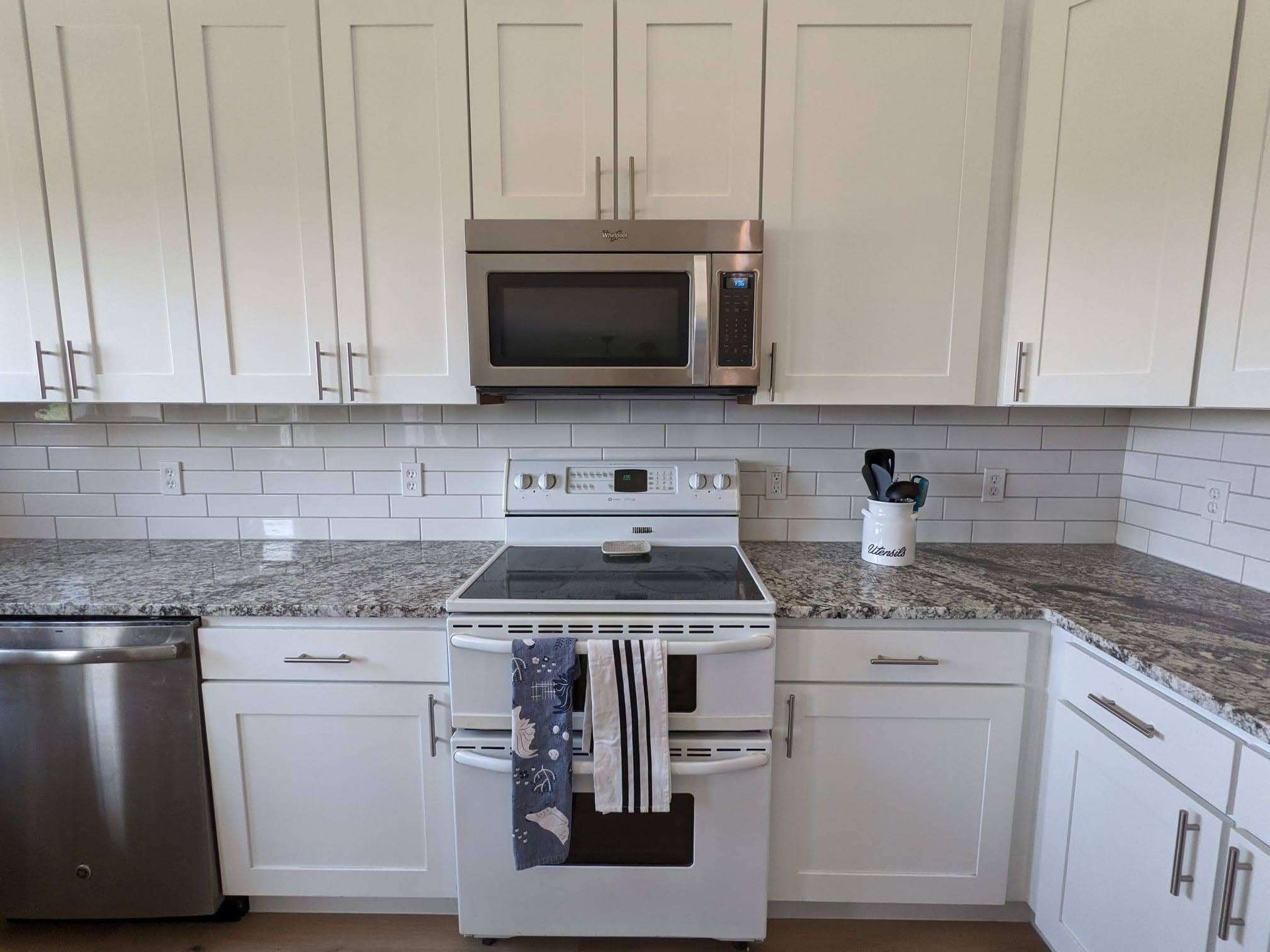 White kitchen with granite countertops, stainless steel appliances, and white subway tile backsplash.