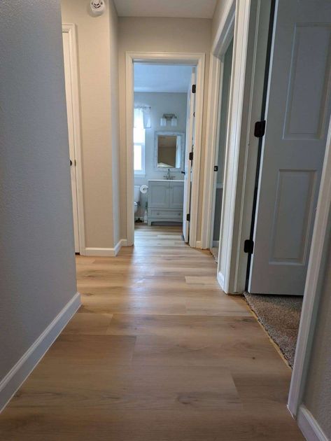 Hallway with light wood flooring, white doors, and a bathroom at the end.