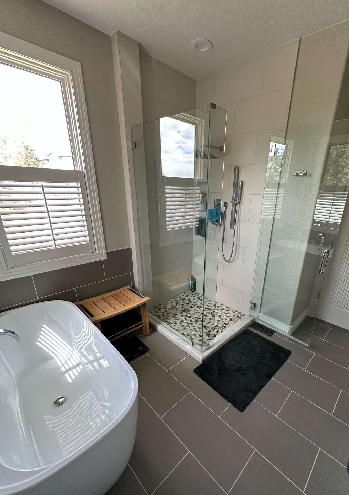 Modern bathroom with a walk-in shower, soaking tub, and a window with shutters.