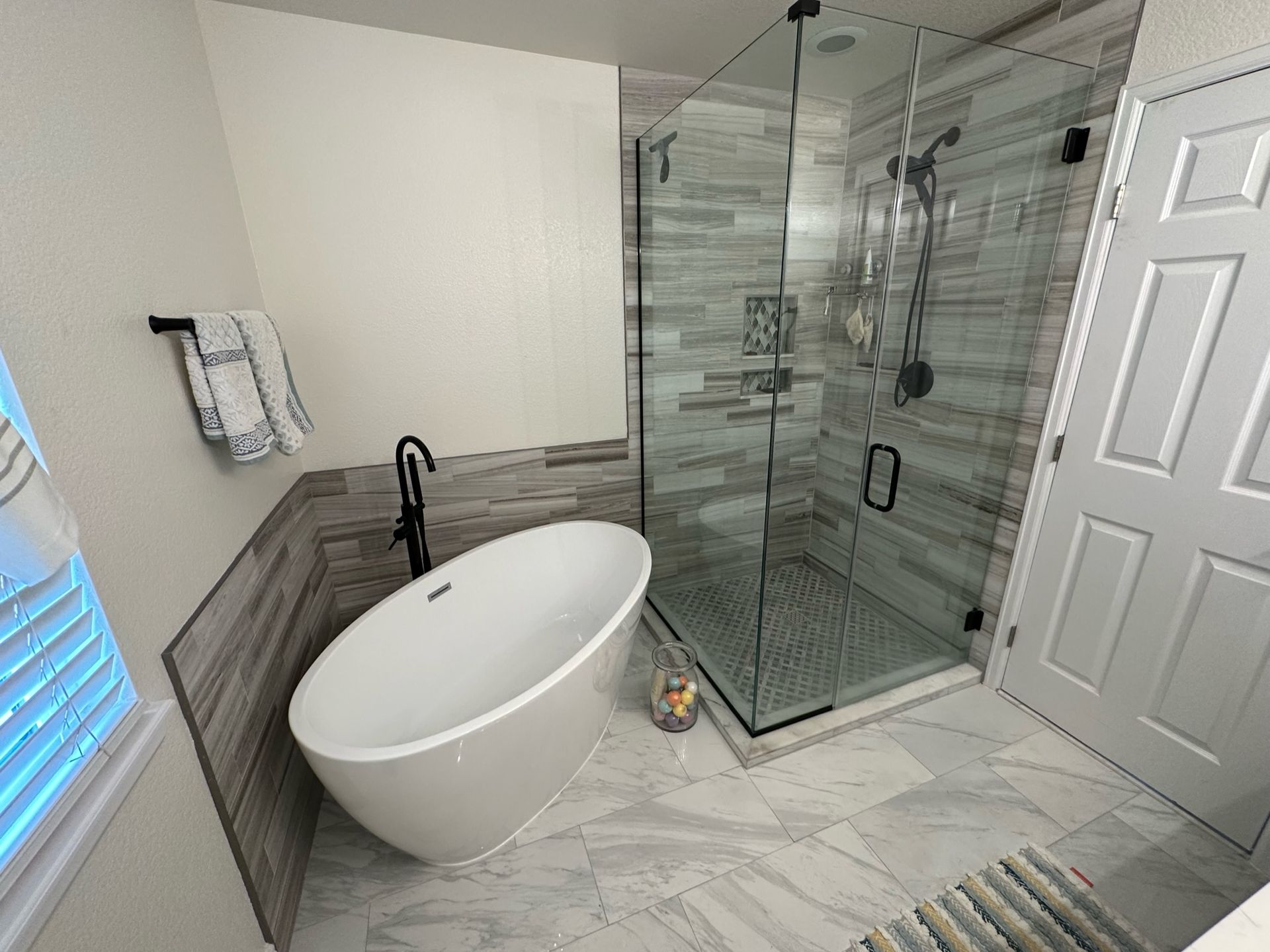 Modern bathroom with a tub, glass shower, white walls, and gray tile flooring.
