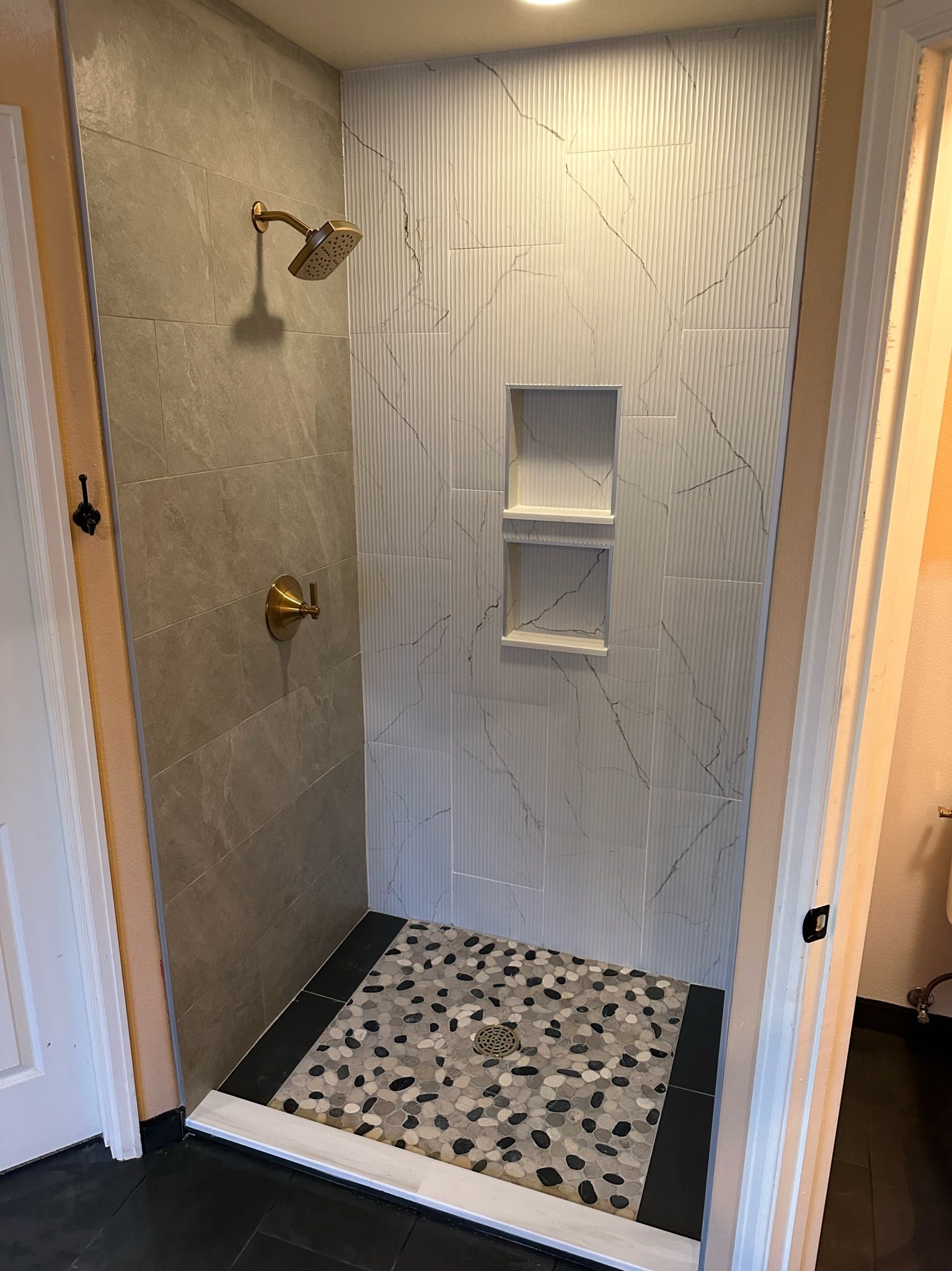 A walk-in shower with gray and white tile, pebble floor, and bronze fixtures.