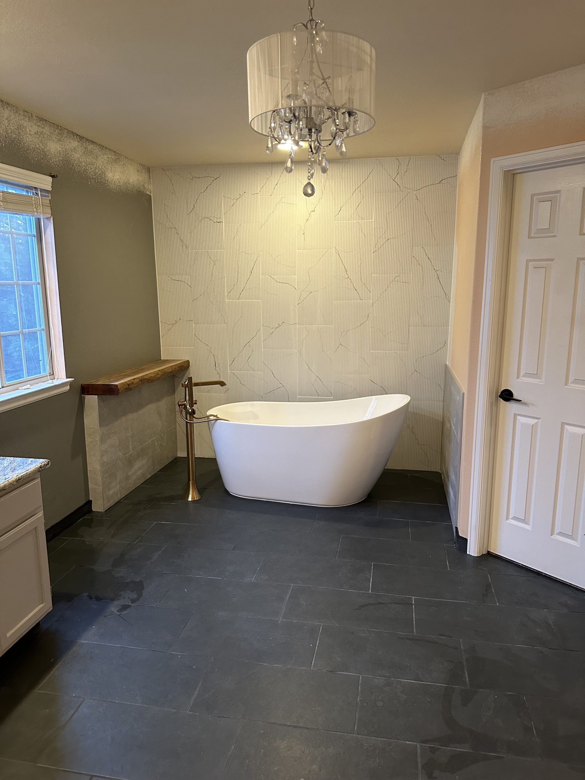 Bathroom with a white tub, chandelier, and dark floor.