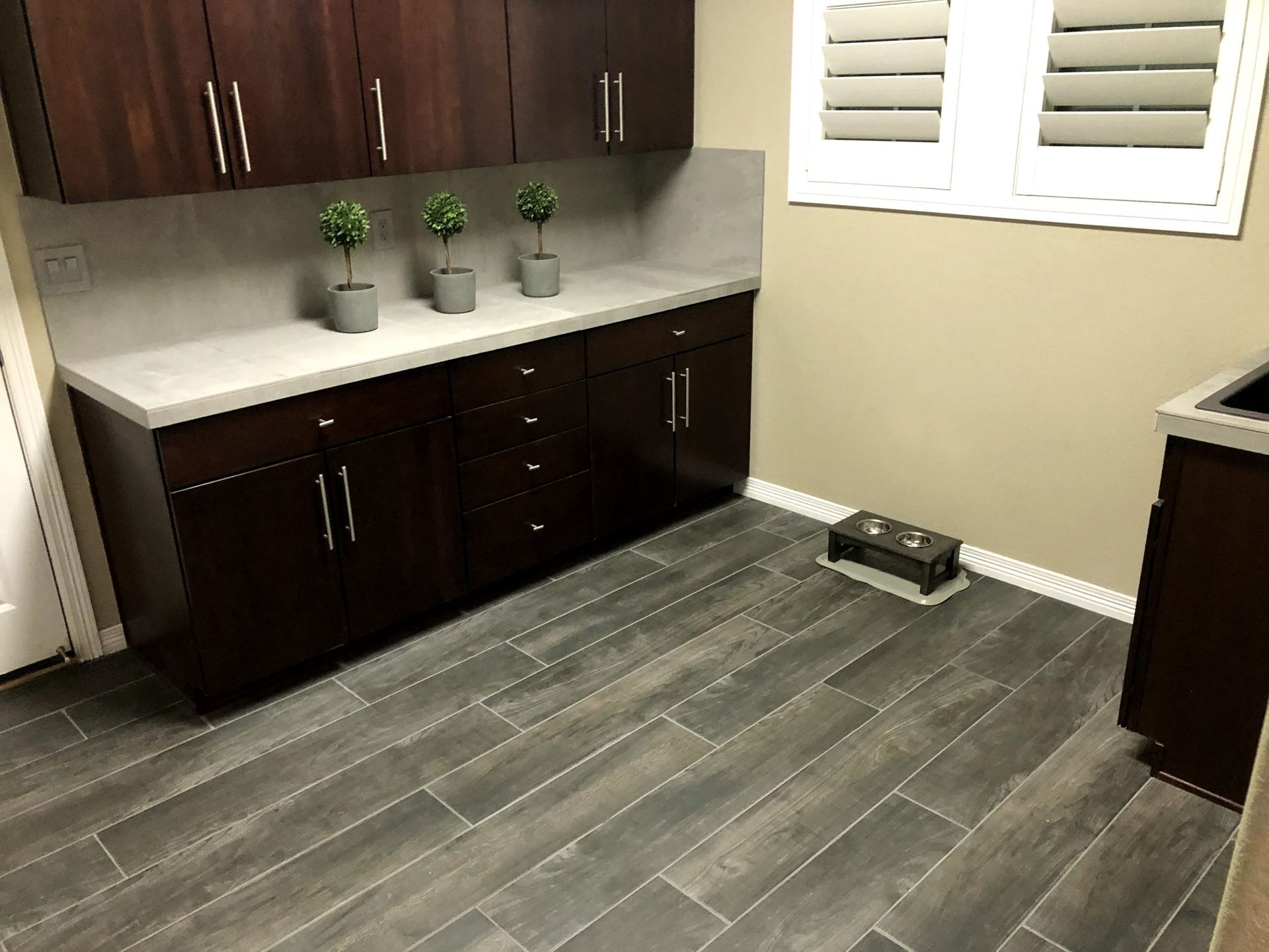 Dark wood cabinets and countertops in a room with gray tile flooring. Three small potted plants sit on the counter.