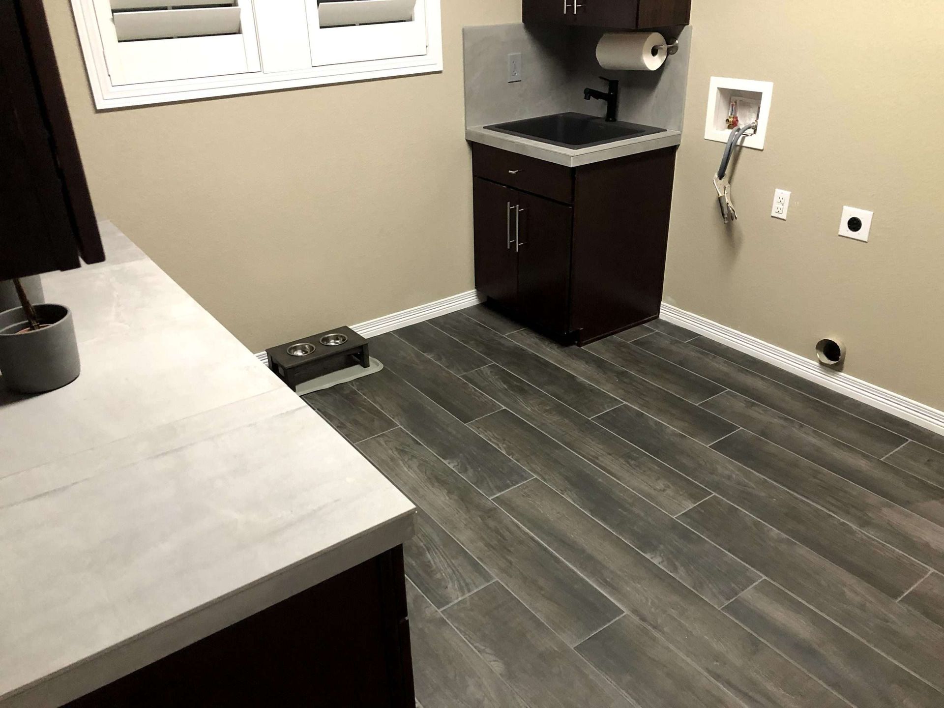 Laundry room with dark brown cabinets, grey wood-look floor, washing machine hookup, and a window.
