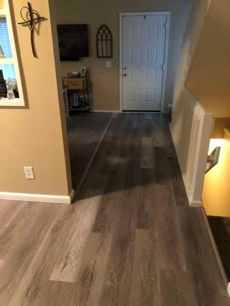 Entryway with wood-look flooring, beige walls, white trim. Front door is visible, staircase on the right.