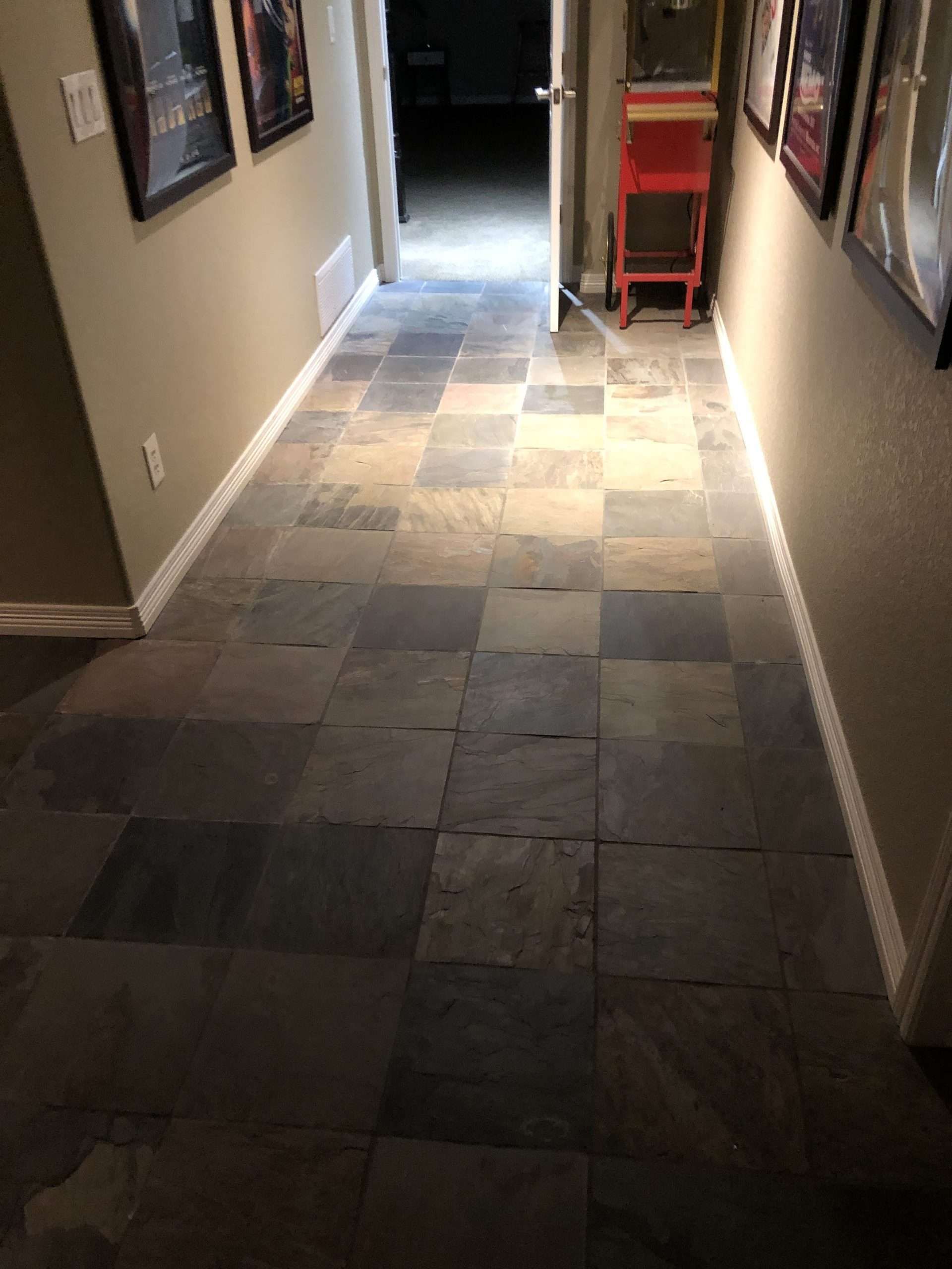 Hallway with checkered slate tile floor, framed photos on walls, and open door.