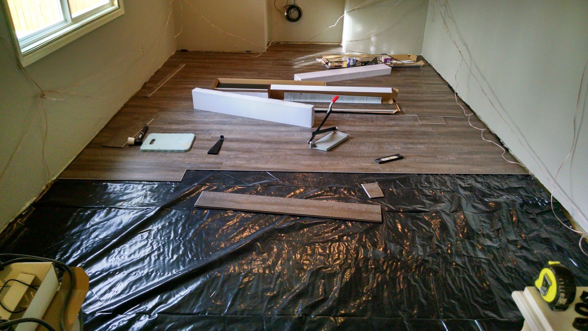 Room with wood-look flooring installation in progress; dark plastic covers floor.