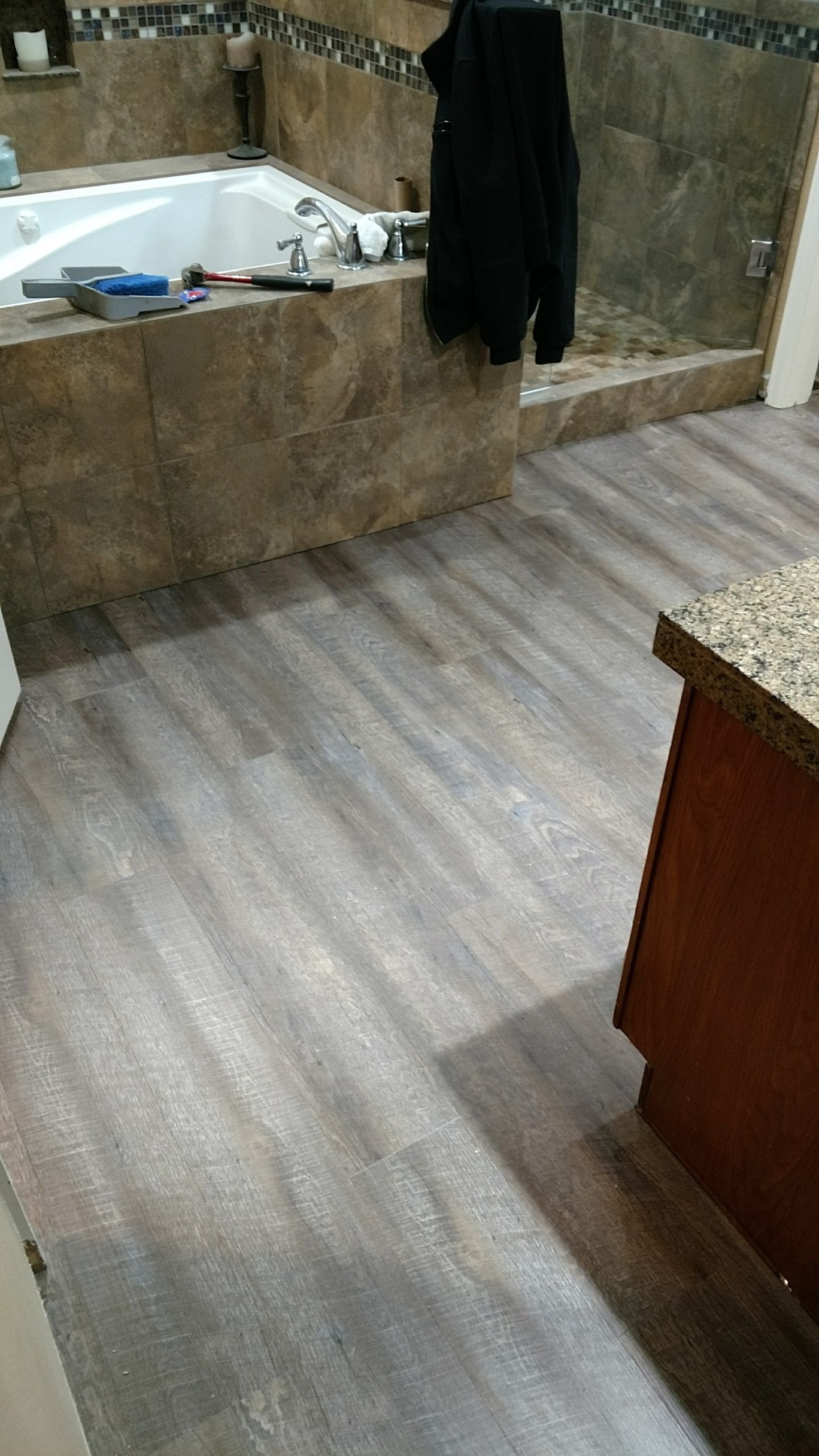 Bathroom with new wood-look flooring, a jacuzzi tub, and brown tile walls. A cabinet and a jacket are visible.